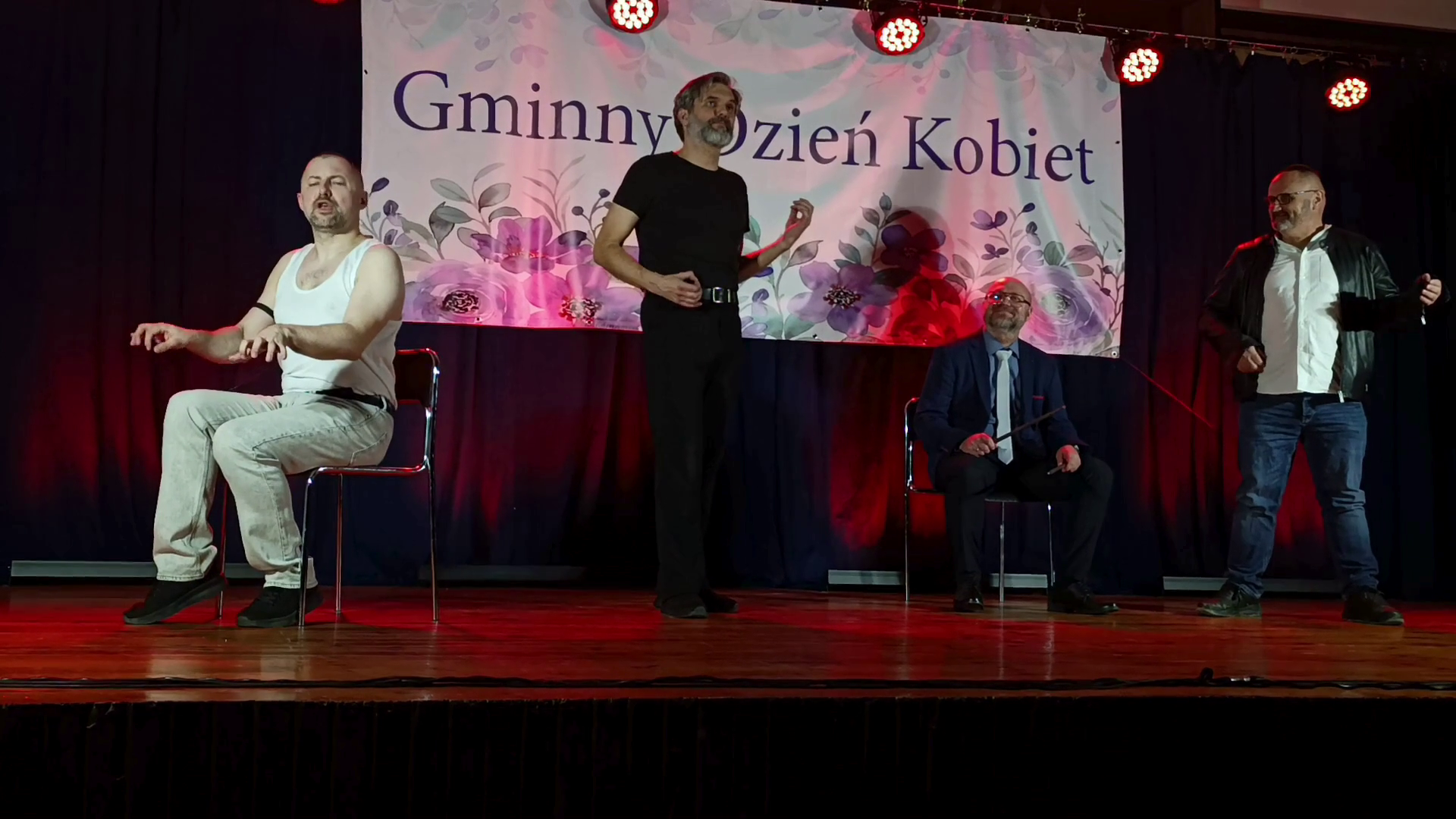 Czterech mężczyzn na scenie podczas występu na wydarzeniu „Gminny Dzień Kobiet”; w tle baner z nazwą wydarzenia