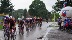 Peleton kolarek uczestniczących w 4. Tour de Pologne Women przejeżdża przez skrzyżowanie w Gorajcu-Starej Wsi na terenie Gminy Radecznica. Przy drodze kibicują mieszkańcy oraz członkowie Brygady RR – Rowerowej Radecznica z flagami i balonem promocyjnym gminy. Nad bezpieczeństwem wyścigu czuwają strażacy i służby porządkowe. Nawierzchnia jezdni jest mokra po opadach deszczu.